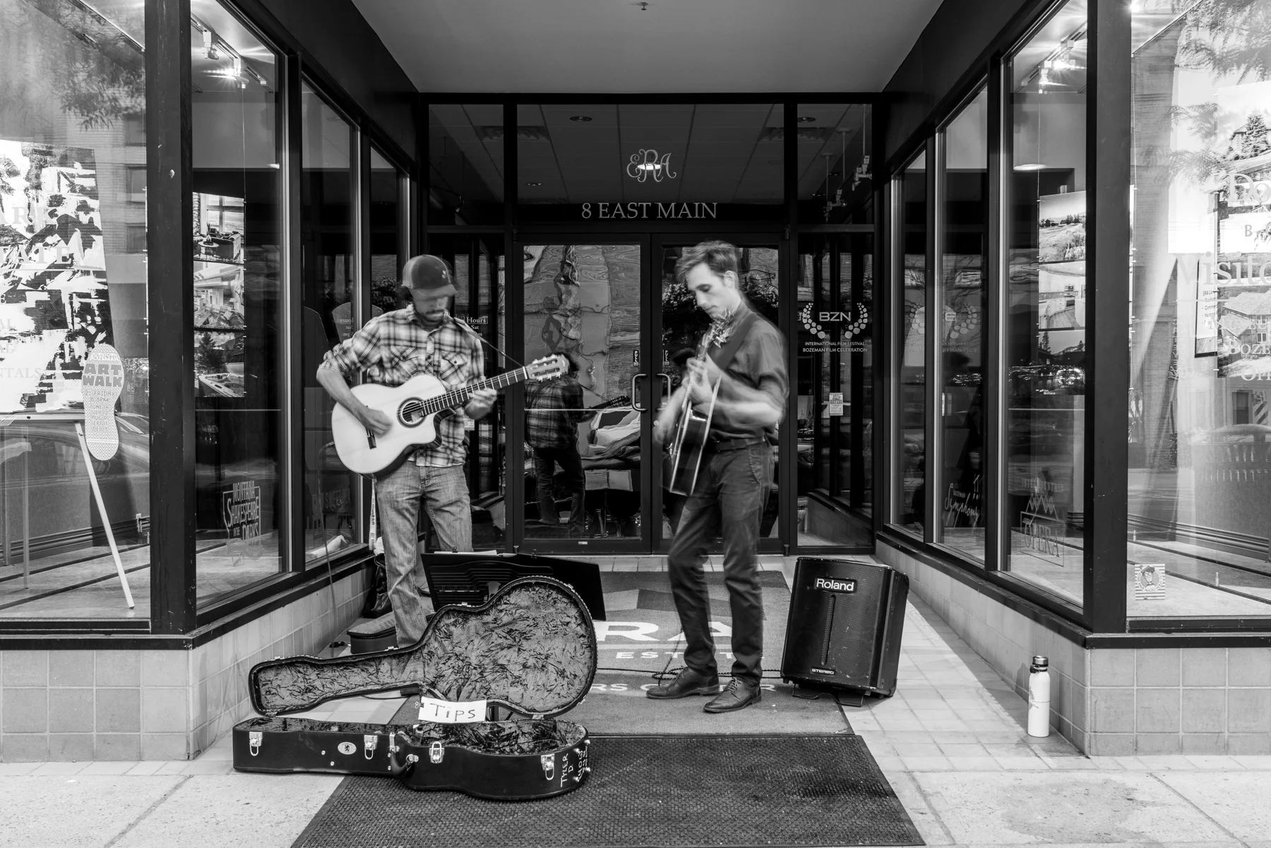 Two musicians playing guitars outside a downtown Bozeman storefront